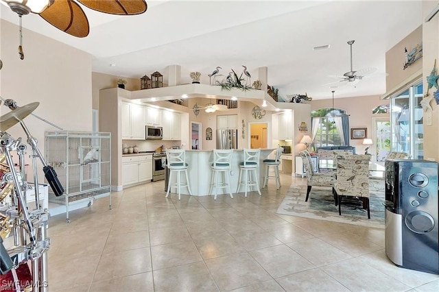 interior space with a breakfast bar, light tile patterned floors, stainless steel appliances, and a ceiling fan