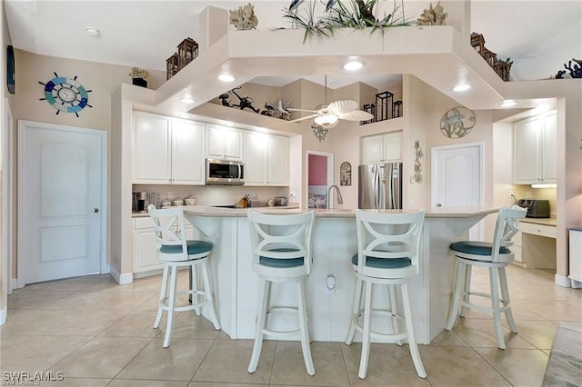 kitchen with white cabinets, a breakfast bar area, stainless steel appliances, light countertops, and a sink