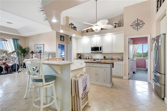 kitchen featuring appliances with stainless steel finishes, light tile patterned floors, a kitchen island, and a ceiling fan