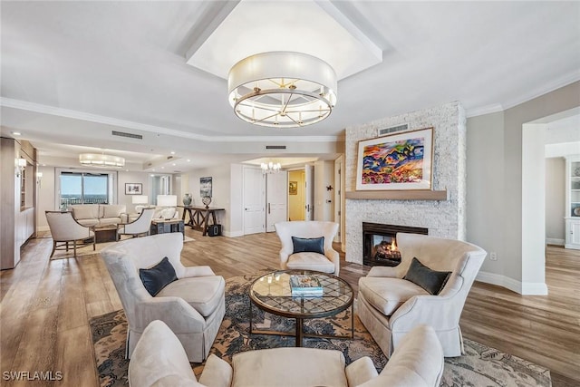 living room featuring wood-type flooring, a fireplace, ornamental molding, and a notable chandelier