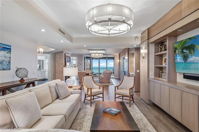 living room featuring crown molding, a notable chandelier, a tray ceiling, light hardwood / wood-style flooring, and built in features