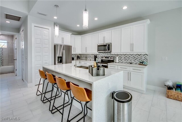 kitchen featuring appliances with stainless steel finishes, white cabinetry, sink, hanging light fixtures, and a kitchen island with sink