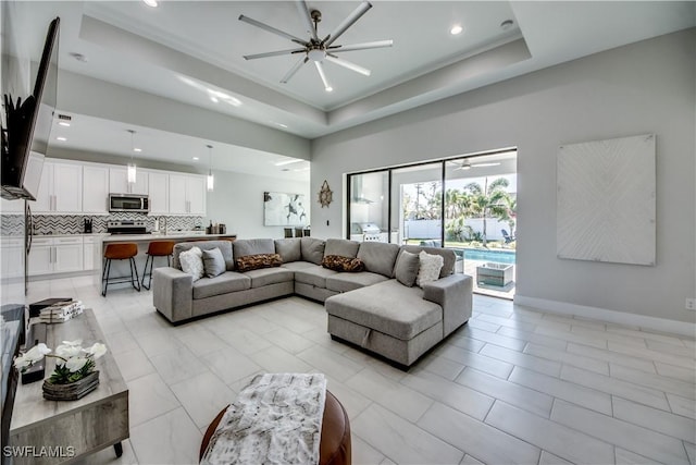 living room with ceiling fan, sink, and a tray ceiling