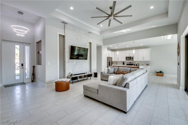 living room with a raised ceiling and ceiling fan with notable chandelier