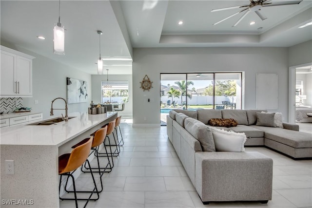 living room with ceiling fan, plenty of natural light, a raised ceiling, and sink