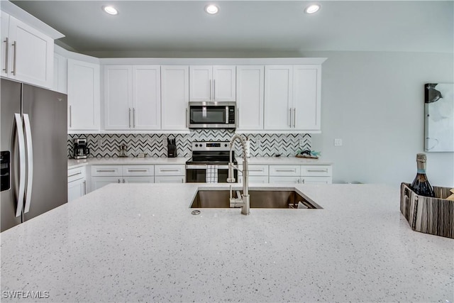 kitchen featuring appliances with stainless steel finishes, sink, light stone counters, and white cabinetry