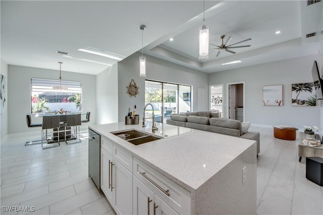 kitchen featuring white cabinetry, a tray ceiling, a kitchen island with sink, pendant lighting, and sink