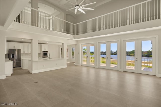 unfurnished living room featuring a towering ceiling, french doors, ceiling fan, and a water view