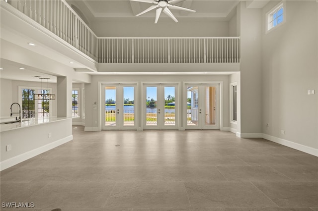 unfurnished living room with a high ceiling, ceiling fan, a healthy amount of sunlight, and sink