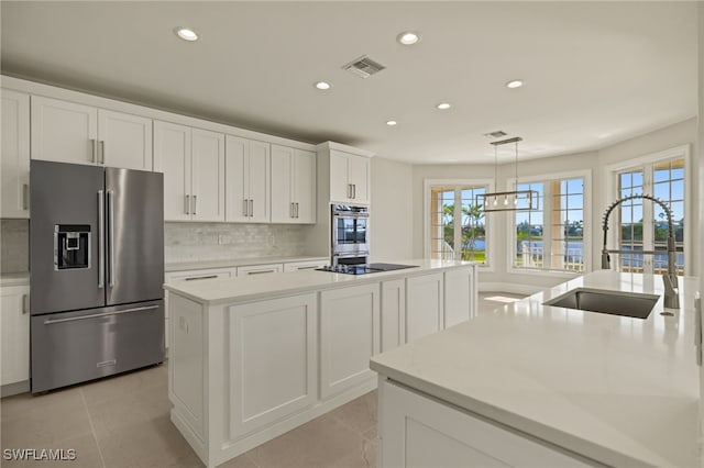 kitchen featuring white cabinets, stainless steel appliances, an island with sink, sink, and decorative light fixtures