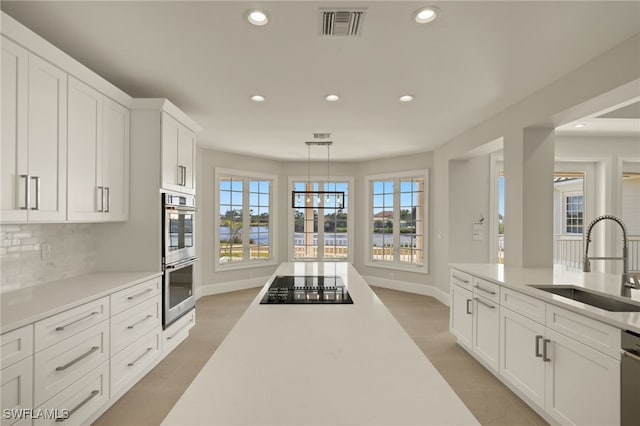 kitchen featuring decorative light fixtures, black electric cooktop, double oven, white cabinets, and sink