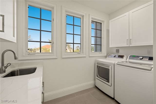 clothes washing area with sink, washing machine and clothes dryer, light tile patterned floors, and cabinets