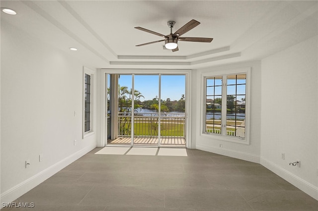 unfurnished room with ceiling fan, a water view, and a raised ceiling