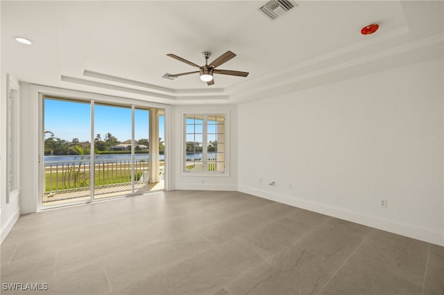 empty room with ceiling fan, a water view, and a raised ceiling