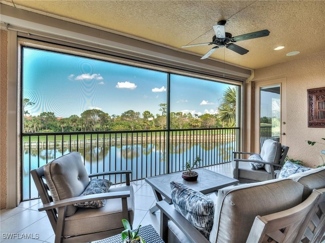 sunroom with ceiling fan and a water view