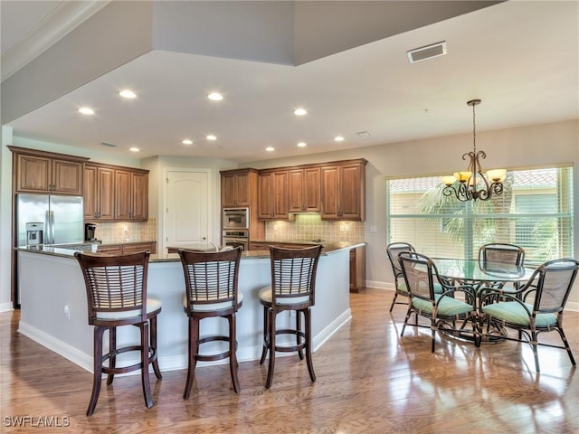 kitchen featuring a large island with sink, dark stone counters, stainless steel fridge with ice dispenser, hanging light fixtures, and a chandelier