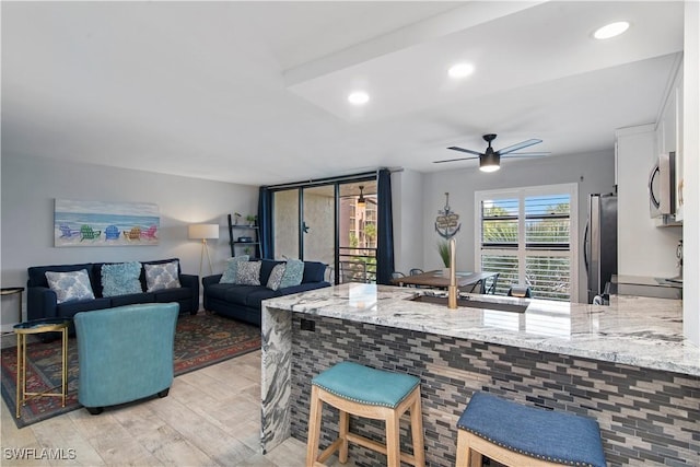 kitchen featuring stainless steel appliances, kitchen peninsula, ceiling fan, light stone counters, and white cabinets