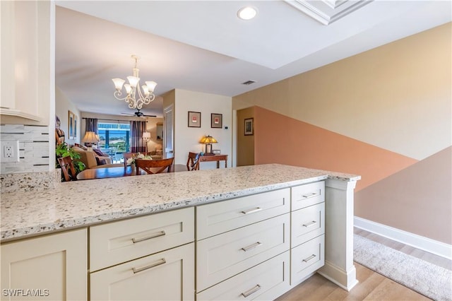 kitchen featuring light hardwood / wood-style floors, kitchen peninsula, tasteful backsplash, and light stone countertops