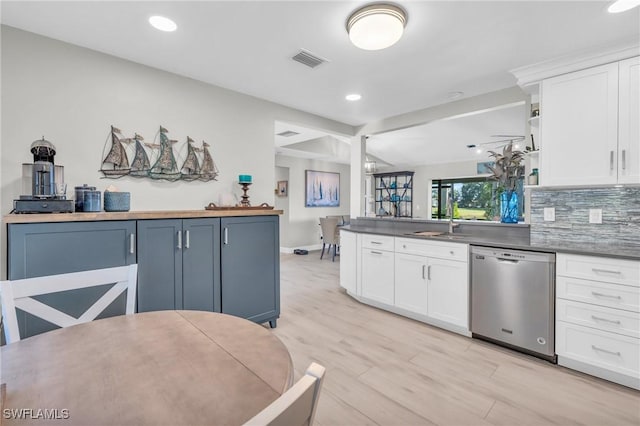 kitchen with sink, tasteful backsplash, light wood-type flooring, stainless steel dishwasher, and white cabinets