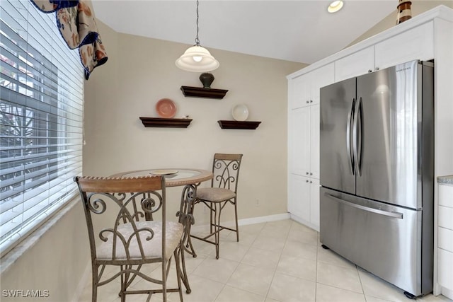 kitchen with light tile patterned floors, stainless steel refrigerator, vaulted ceiling, pendant lighting, and white cabinets