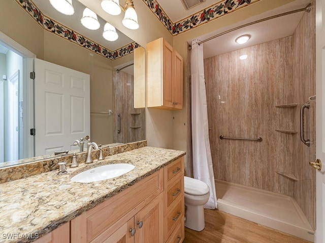 bathroom with hardwood / wood-style floors, toilet, walk in shower, and vanity