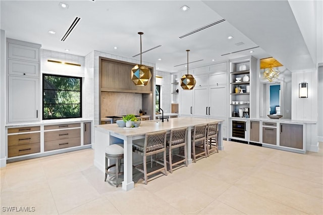 kitchen featuring a kitchen breakfast bar, wine cooler, a large island with sink, and decorative light fixtures