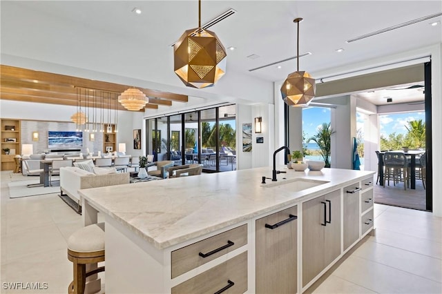 kitchen featuring light stone countertops, pendant lighting, an island with sink, light brown cabinetry, and sink