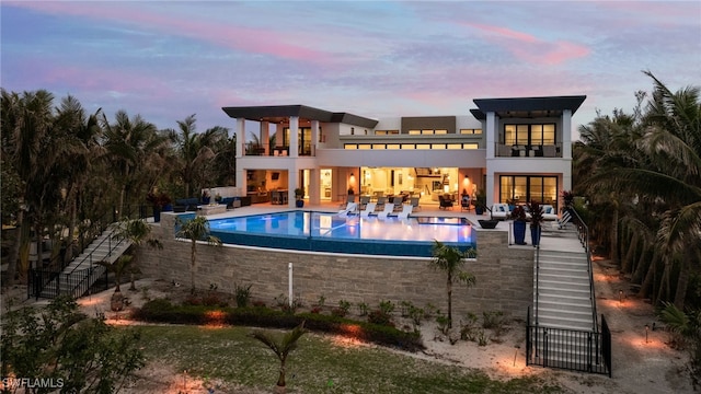 back house at dusk featuring a balcony, an outdoor hangout area, and a patio