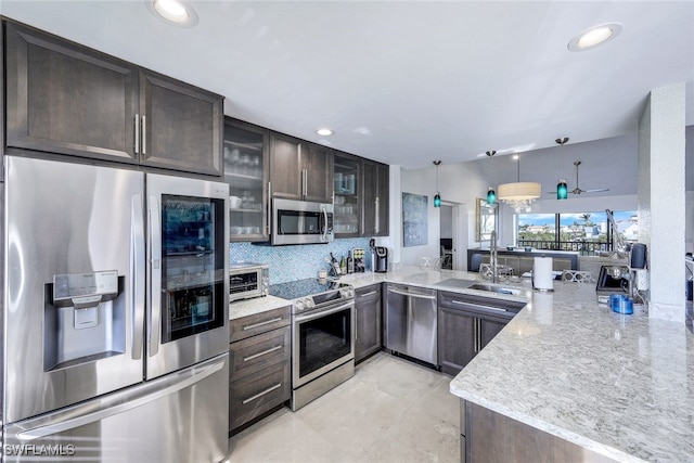 kitchen with kitchen peninsula, stainless steel appliances, tasteful backsplash, hanging light fixtures, and light stone counters