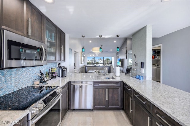 kitchen with pendant lighting, appliances with stainless steel finishes, washing machine and clothes dryer, sink, and kitchen peninsula