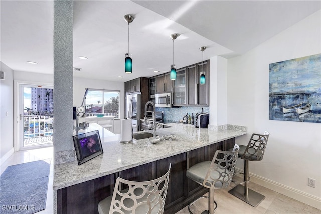 kitchen featuring kitchen peninsula, stainless steel appliances, tasteful backsplash, a kitchen breakfast bar, and dark brown cabinetry