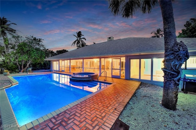 pool at dusk featuring an in ground hot tub