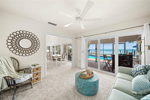 carpeted living room featuring a water view and ceiling fan