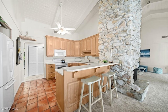 kitchen featuring white appliances, a breakfast bar area, kitchen peninsula, beamed ceiling, and light brown cabinets