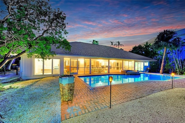 pool at dusk with an in ground hot tub and a patio