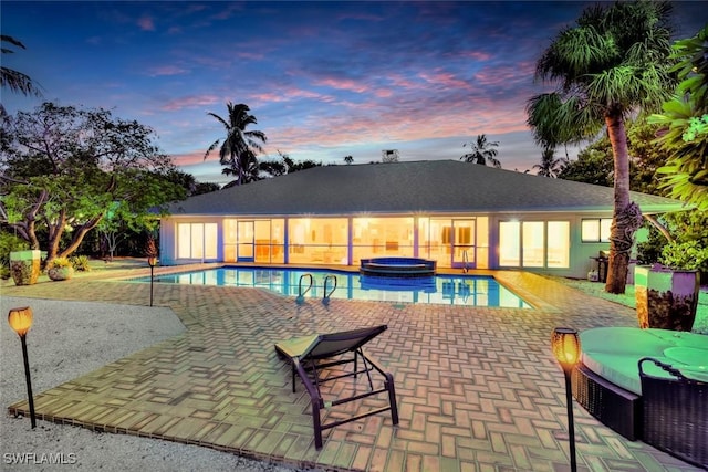 pool at dusk featuring a patio area and an in ground hot tub