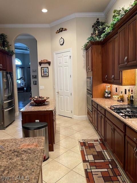 kitchen featuring light stone counters, a center island, stainless steel appliances, ornamental molding, and light tile patterned flooring