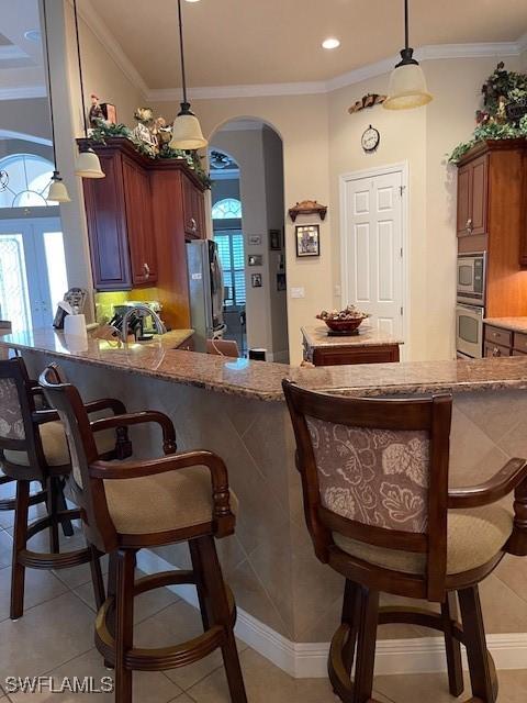 kitchen with decorative light fixtures, a kitchen bar, light tile patterned floors, crown molding, and appliances with stainless steel finishes