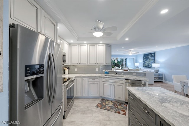 kitchen with light stone countertops, appliances with stainless steel finishes, sink, gray cabinets, and a raised ceiling