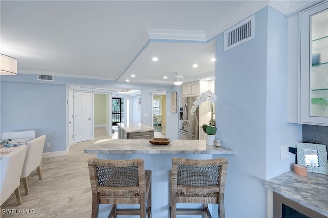 kitchen with crown molding, stainless steel fridge, a kitchen breakfast bar, and white cabinets