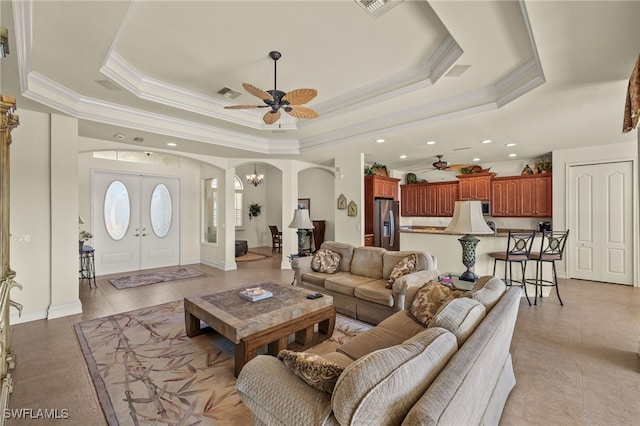 tiled living room with ornamental molding, ceiling fan with notable chandelier, and a tray ceiling