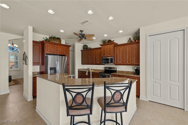 kitchen featuring a breakfast bar area, light tile patterned floors, appliances with stainless steel finishes, an island with sink, and ceiling fan with notable chandelier