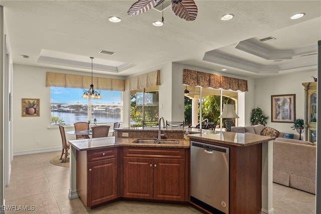 kitchen with sink, a kitchen island with sink, hanging light fixtures, a tray ceiling, and stainless steel dishwasher