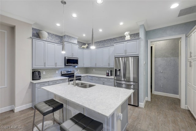 kitchen with pendant lighting, sink, appliances with stainless steel finishes, an island with sink, and decorative backsplash