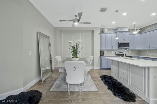 kitchen featuring pendant lighting, sink, light stone countertops, an island with sink, and decorative backsplash