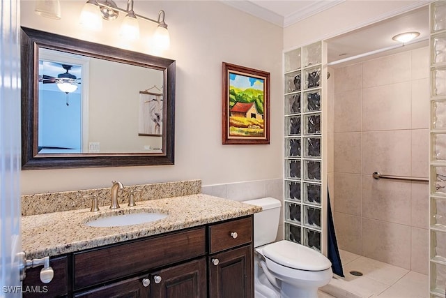 bathroom with toilet, a tile shower, ceiling fan, ornamental molding, and vanity