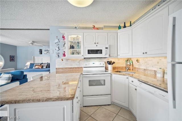 kitchen with light tile patterned flooring, a peninsula, white appliances, a sink, and white cabinetry