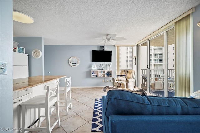 living area featuring a ceiling fan, light tile patterned flooring, a textured ceiling, a wall of windows, and baseboards