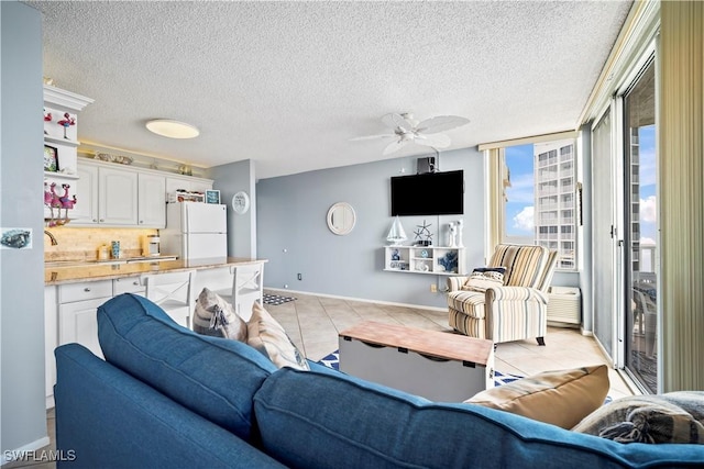 living room featuring light tile patterned floors, a textured ceiling, baseboards, and a ceiling fan