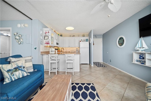 living room with a ceiling fan, a textured ceiling, baseboards, and light tile patterned floors